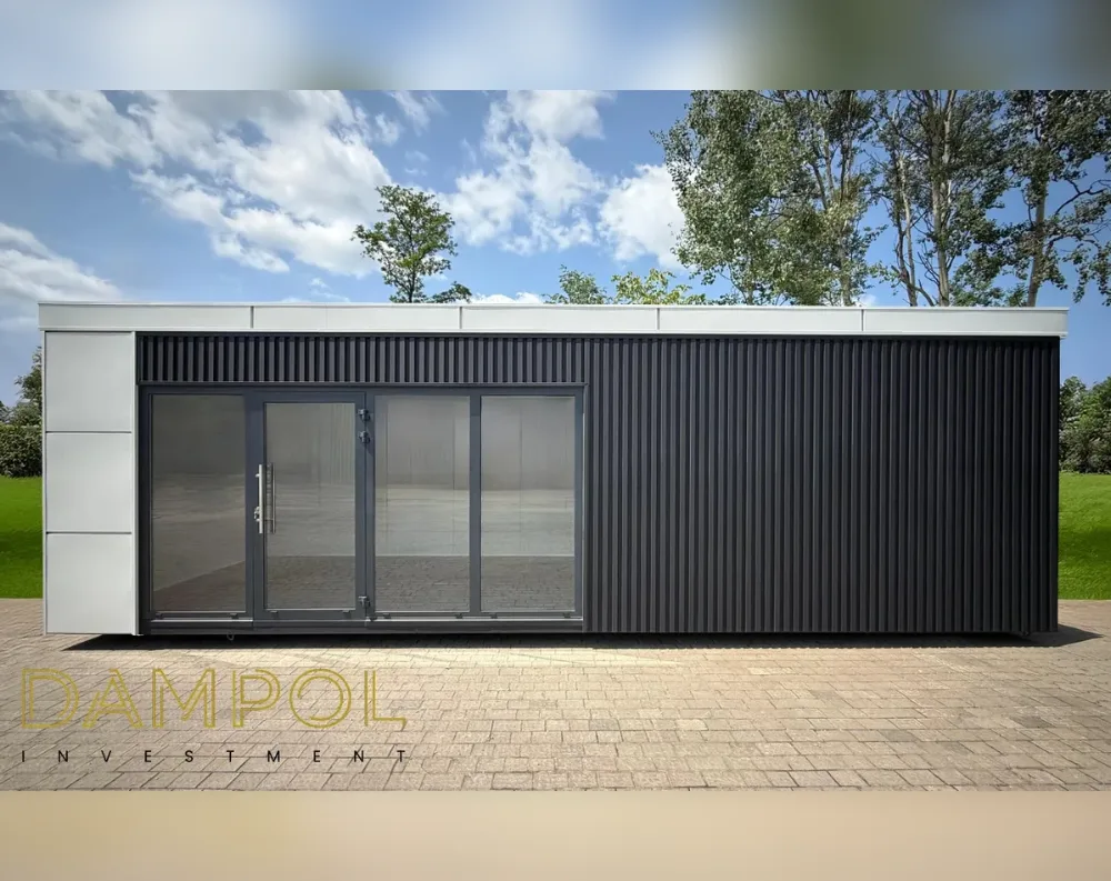 This modular garden office is a long, low rectangular structure with a flat roof topped by a white fascia trim that wraps neatly around the edges. The left-hand third of the front facade is finished in smooth white paneling, while the remainder of the building features dark charcoal-grey vertical slat cladding, giving a striking two-tone contrast. Centered on the white section is a wide glazed entrance: a single hinged glass door paired with a large sliding glass panel beside it, all set within slim dark aluminum frames, allowing full visibility into the empty interior. The right two-thirds of the structure is a solid, windowless expanse of ribbed dark paneling, giving it a sleek, minimalist, contemporary appearance.