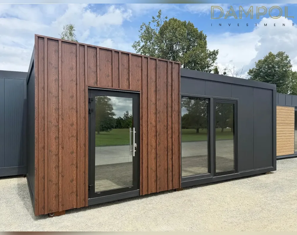 This modular garden building has a rectangular, single-story footprint with a flat roof and low-profile proportions, wider than it is tall. The left-facing gable end is clad in vertical dark walnut-toned wood-effect paneling, contrasting with the smooth charcoal-grey composite panels covering the rest of the structure. A tall glass-paneled entry door with black framing and a modern handle sits within the wooden section, while the adjacent grey wall features a wide double sliding glass door system with slim black frames, offering an unobstructed view. The corners appear crisply finished, giving it a sleek, contemporary aesthetic suited for a home office or garden studio.