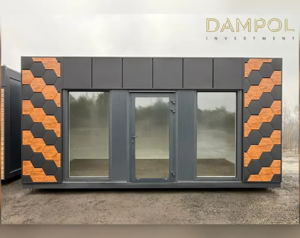 This modular garden office is a long, low, rectangular unit with a flat roof and a sleek, contemporary silhouette. Its façade is clad in dark charcoal-grey panels, giving it a sharp, modern look. Centered on the front are two large fixed glass windows flanking a single glazed entry door with a slim metal frame and handle. Above the windows and door runs a band of paneled trim in matching grey. On both far ends of the building, eye-catching hexagonal tiles in a mix of black and warm wood-tone orange create a bold, geometric accent, adding visual interest and contrast to the otherwise minimalist, industrial-style exterior.