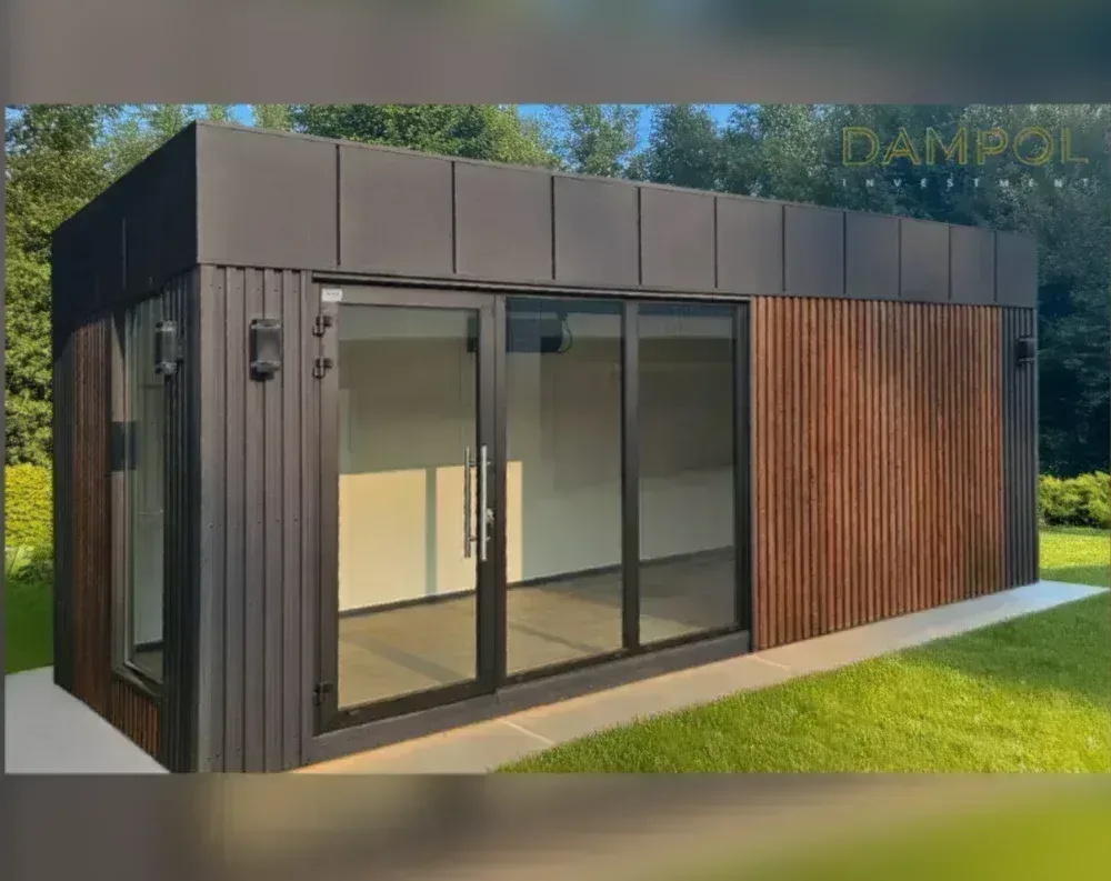 This modern garden office is a low, rectangular single-story structure with a flat roof, photographed at an angle showing its front and side. The upper facade and roofline are clad in smooth dark brown horizontal panels, while the lower portion features vertical slatted wood cladding—dark charcoal tones on the left side and a warmer, natural wood finish on the right. The centerpiece is a large glass entrance system: a hinged door with a sleek vertical handle paired with a wide sliding glass panel beside it, both set in slim black frames. A small window is visible on the far left wall. The building sits on a concrete slab bordered by trimmed green lawn, with trees visible behind it.